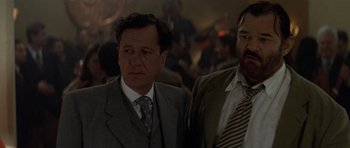 Movie still from “The Tailor of Panama” (2001), directed by John Boorman – A man in a suit and tie standing next to another man in a suit and tie; Close Up shot, Low angle