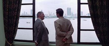 Movie still from “The Tailor of Panama” (2001), directed by John Boorman – Two men in suits looking out of a window; Medium shot, Over the shoulder angle