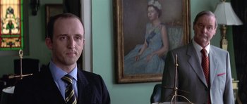 Movie still from “The Tailor of Panama” (2001), directed by John Boorman – A man sitting in front of a painting of a woman; Close Up shot, Low angle