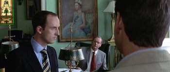 Movie still from “The Tailor of Panama” (2001), directed by John Boorman – A group of men sitting at a table in front of a painting; Close Up shot, Over the shoulder angle