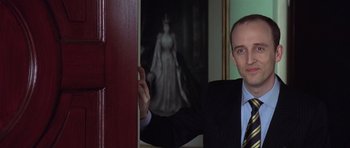 Movie still from “The Tailor of Panama” (2001), directed by John Boorman – A man standing in front of a picture of a woman; Close Up shot, Low angle