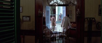 Movie still from “The Tailor of Panama” (2001), directed by John Boorman – Three people standing at a table looking out a window; Wide shot, High angle