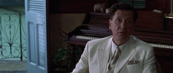 Movie still from “The Tailor of Panama” (2001), directed by John Boorman – A man wearing a white suit sitting in front of a piano; Close Up shot, Low angle