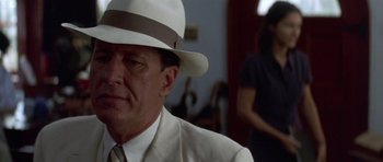 Movie still from “The Tailor of Panama” (2001), directed by John Boorman – A man wearing a white suit and a white hat; Close Up shot, Over the shoulder angle