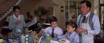Movie still from “The Tailor of Panama” (2001), directed by John Boorman – A boy and a girl sitting at a table eating breakfast; Medium shot, Over the shoulder angle