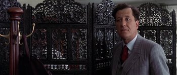 Movie still from “The Tailor of Panama” (2001), directed by John Boorman – A man standing in front of an intricately carved screen; Close Up shot, Over the shoulder angle