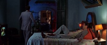 Movie still from “The Tailor of Panama” (2001), directed by John Boorman – A person laying on a bed in front of a fire place; Wide shot, High angle