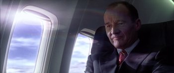 Movie still from “The Tailor of Panama” (2001), directed by John Boorman – A man wearing a suit and tie sitting in a plane; Close Up shot, Low angle