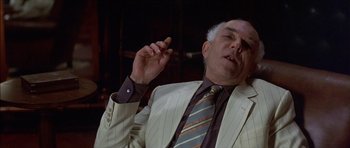 Movie still from “The Tailor of Panama” (2001), directed by John Boorman – An older man in a suit and tie smoking a cigarette; Close Up shot, Low angle