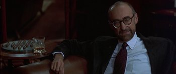 Movie still from “The Tailor of Panama” (2001), directed by John Boorman – A man sitting in a chair wearing a suit and tie; Close Up shot, Over the shoulder angle