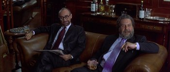 Movie still from “The Tailor of Panama” (2001), directed by John Boorman – Two men in suits sitting on a leather couch; Medium shot, High angle