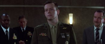 Movie still from “The Tailor of Panama” (2001), directed by John Boorman – A man in a military uniform standing in front of a wall; Medium shot, Over the shoulder angle