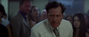 Movie still from “The Tailor of Panama” (2001), directed by John Boorman – A man in a white suit and a green tie; Close Up shot, Over the shoulder angle