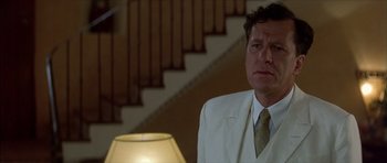 Movie still from “The Tailor of Panama” (2001), directed by John Boorman – A man wearing a suit and tie standing next to a lamp; Close Up shot, Low angle