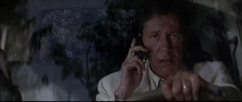Movie still from “The Tailor of Panama” (2001), directed by John Boorman – A man talking on a cell phone while sitting down; Close Up shot, Low angle