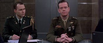 Movie still from “The Tailor of Panama” (2001), directed by John Boorman – A man in a military uniform sitting next to another man; Medium shot, Low angle