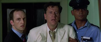 Movie still from “The Tailor of Panama” (2001), directed by John Boorman – A person wearing a suit and tie; Close Up shot, Over the shoulder angle