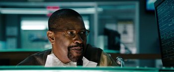 Movie still from “The Taking of Pelham 123” (2009), directed by Tony Scott – A man with glasses is sitting at a podium; Close Up shot, Over the shoulder angle