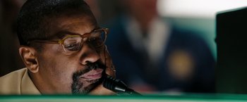 Movie still from “The Taking of Pelham 123” (2009), directed by Tony Scott – A man with glasses is sitting at a microphone; Close Up shot, Over the shoulder angle