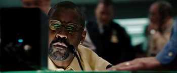 Movie still from “The Taking of Pelham 123” (2009), directed by Tony Scott – An older man wearing glasses is speaking into a microphone; Close Up shot, Low angle
