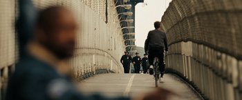 Movie still from “The Taking of Pelham 123” (2009), directed by Tony Scott – A man riding a bike down a street next to a fence; Extreme Wide shot, Over the shoulder angle