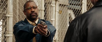 Movie still from “The Taking of Pelham 123” (2009), directed by Tony Scott – A man holding a gun while standing in front of a fence; Close Up shot, Over the shoulder angle