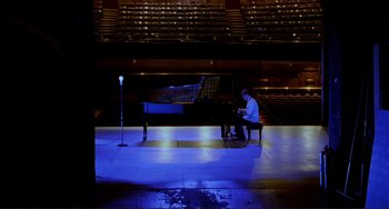 Movie still from “The Talented Mr. Ripley” (1999), directed by Anthony Minghella – A man sitting on a bench playing a piano in an auditorium; Extreme Wide shot, High angle