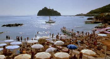 Movie still from “The Talented Mr. Ripley” (1999), directed by Anthony Minghella – A group of people sitting on the beach under umbrellas; Extreme Wide shot, High angle