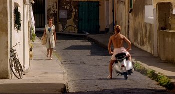 Movie still from “The Talented Mr. Ripley” (1999), directed by Anthony Minghella – A man riding a scooter down the middle of a street; Wide shot, Over the shoulder angle