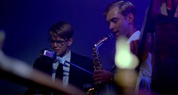 Movie still from “The Talented Mr. Ripley” (1999), directed by Anthony Minghella – Two men in suits and ties playing a saxophone and a microphone; Close Up shot, Low angle
