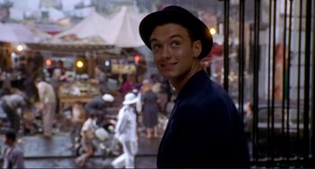 Movie still from “The Talented Mr. Ripley” (1999), directed by Anthony Minghella – A young man wearing a black hat standing in front of a crowd of onlookers; Close Up shot, Over the shoulder angle