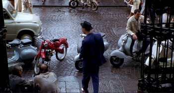 Movie still from “The Talented Mr. Ripley” (1999), directed by Anthony Minghella – A man standing next to two motorcycles on a street; Wide shot, High angle