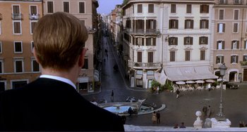 Movie still from “The Talented Mr. Ripley” (1999), directed by Anthony Minghella – A man standing on a balcony looking down at a street; Extreme Wide shot, Over the shoulder angle