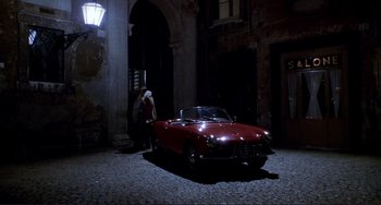 Movie still from “The Talented Mr. Ripley” (1999), directed by Anthony Minghella – A red car parked in front of a building at night; Wide shot, High angle