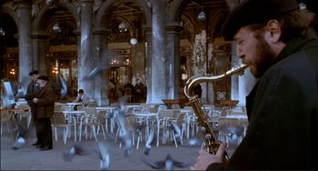 Movie still from “The Talented Mr. Ripley” (1999), directed by Anthony Minghella – A man playing a saxophone in an open air cafe; Wide shot, High angle