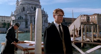 Movie still from “The Talented Mr. Ripley” (1999), directed by Anthony Minghella – A man in a suit and tie standing in front of a building; Medium shot, Low angle