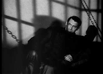 Movie still from “The Talk of the Town” (1942), directed by George Stevens – A black and white photo of a man sitting in front of bars; Medium shot, High angle