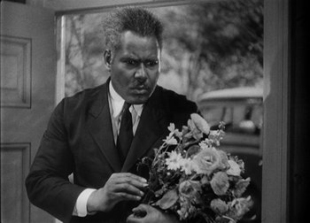 Movie still from “The Talk of the Town” (1942), directed by George Stevens – A black and white photo of a man holding a bouquet of flowers; Medium shot, Low angle