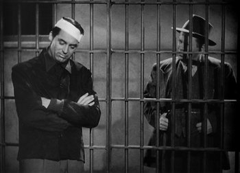 Movie still from “The Talk of the Town” (1942), directed by George Stevens – A man with bandage on his head standing next to another man in jail; Medium shot, Low angle
