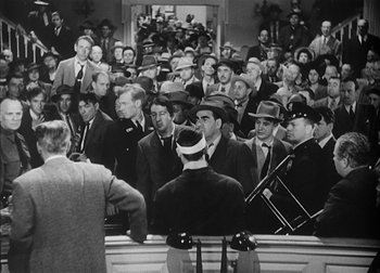 Movie still from “The Talk of the Town” (1942), directed by George Stevens – A group of men in suits and hats sitting in front of a group of people; Wide shot, High angle