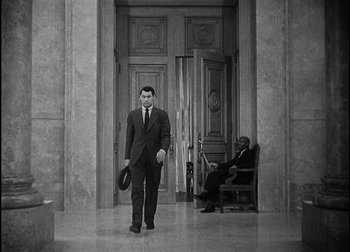 Movie still from “The Talk of the Town” (1942), directed by George Stevens – A man in a suit and hat walking in front of a chair; Wide shot, High angle