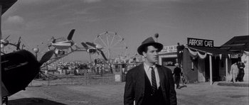 Movie still from “The Tarnished Angels” (1957), directed by Douglas Sirk – A black and white photo of a man in a suit and hat; Medium shot, Low angle