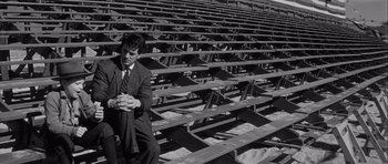 Movie still from “The Tarnished Angels” (1957), directed by Douglas Sirk – A black and white photo of a man sitting in a bleacher; Wide shot, High angle