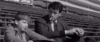 Movie still from “The Tarnished Angels” (1957), directed by Douglas Sirk – A black and white photo of a man smoking a cigarette; Medium shot, Low angle