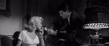 Movie still from “The Tarnished Angels” (1957), directed by Douglas Sirk – A man lighting a cigarette in front of a woman; Medium shot, Low angle