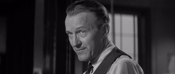 Movie still from “The Tarnished Angels” (1957), directed by Douglas Sirk – An older man wearing a neck tie in a black and white photo; Close Up shot, Low angle