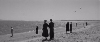 Movie still from “The Tarnished Angels” (1957), directed by Douglas Sirk – Two people standing on the beach looking out at the water; Extreme Wide shot, High angle