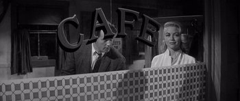 Movie still from “The Tarnished Angels” (1957), directed by Douglas Sirk – A black and white photo of a man and a woman in front of a cafe sign; Medium shot, Over the shoulder angle
