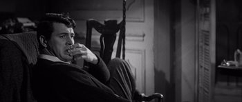 Movie still from “The Tarnished Angels” (1957), directed by Douglas Sirk – A man sitting in a chair eating a sandwich; Medium shot, High angle