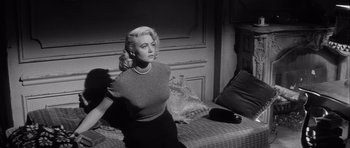 Movie still from “The Tarnished Angels” (1957), directed by Douglas Sirk – A black - and - white photo of a woman sitting on a bed; Medium shot, Low angle